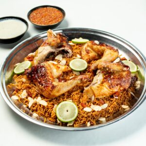 Close-up of chicken biryani with slices of lime, almonds, and sauces on a white background.